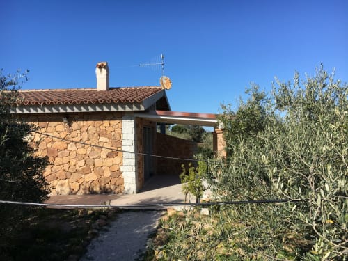 Rustic stone villa in Orosei with terracotta roof, wooden pergola, garden view, and olive trees