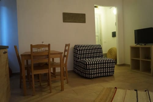 Cozy living room in Orosei villa with wooden dining table, black and white armchair, TV, and tile flooring