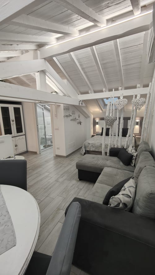 Moderno loft a Ventimiglia con open space, travi bianche, divano grigio, letto a baldacchino e lucernai luminosi
