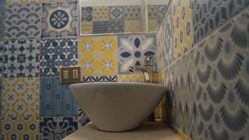 Modern bathroom sink with patterned blue and yellow tiles in Orosei apartment Domo e' Chelu