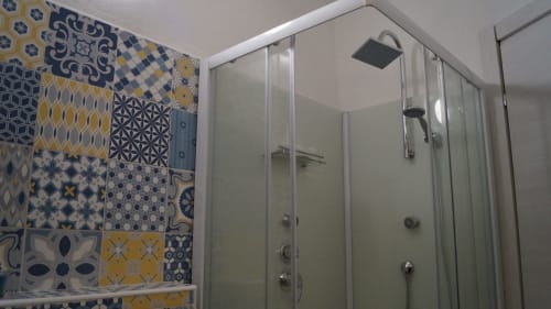 Modern glass shower enclosure with decorative blue and yellow patterned tiles in Orosei apartment bathroom