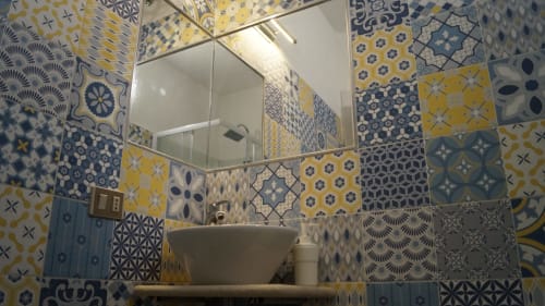 Modern bathroom with blue and yellow patterned tiles, white sink, mirror, and shower in Orosei apartment