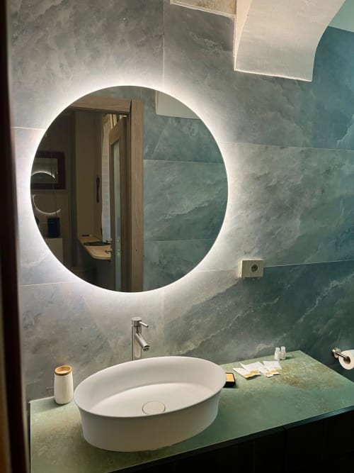 Bagno moderno a San Carlo 104 Caserta con specchio circolare illuminato, pareti in marmo verde e lavabo ovale bianco