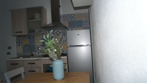 Modern kitchen with blue patterned backtile, stainless steel Beko refrigerator, and wooden table with potted plant at Domo de