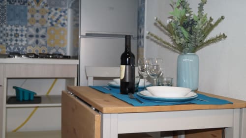 Dining table set with wine bottle, glasses, and place settings in Orosei apartment kitchen with refrigerator and floral