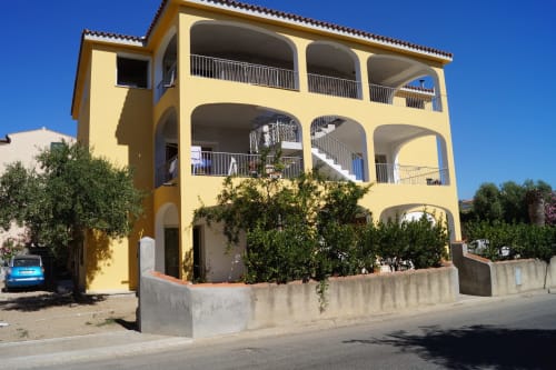 Bright yellow apartment building in Orosei with arched balconies, terraces, and Mediterranean coastal style architecture