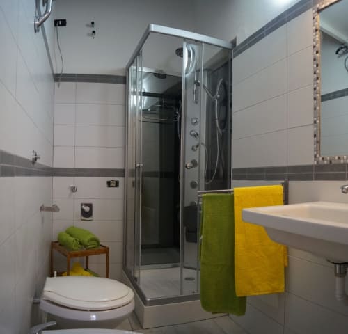 Modern bathroom with shower enclosure, white toilet, sink, and green and yellow towels in Orosei apartment