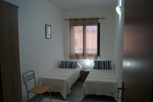 Doppelzimmer in der Wohnung in Orosei mit zwei Einzelbetten, gestreiften Kissen, Fenster mit Vorhängen und minimalistischer Einrichtung