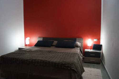 Modernes Schlafzimmer im Sa Domo Mannoi Apartment in Orosei mit roter Akzentwand, Doppelbett, schwarzen Nachttischen und Lesebereich