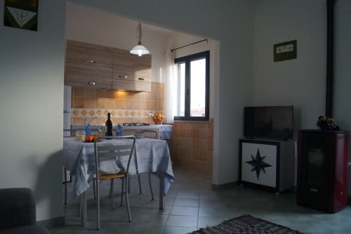 Offene Küche und Essbereich im Apartment in Orosei mit Holzschränken, Terrakotta-Fliesenrückwand und angrenzendem Wohnzimmer