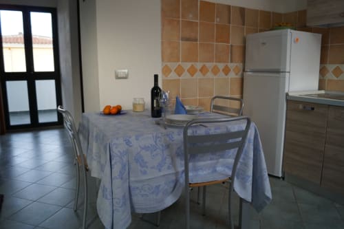 Küchen-Essbereich in der Orosei-Wohnung mit Tisch, Stühlen, weißem Kühlschrank und gefliester Rückwand