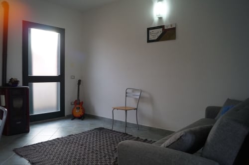 Minimalistisches Wohnzimmer in Orosei mit Gitarre, Sessel, Sofa und hellem Eingangstor