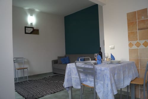 Essbereich mit Tisch und Stühlen im Apartment von Orosei, Sofa und dunkle Akzentwand sichtbar
