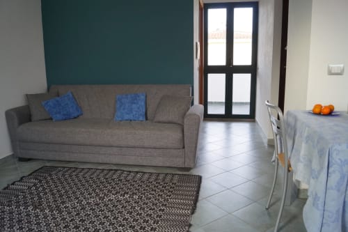 Modernes Wohnzimmer in Orosei mit grauem Sofa, blauen Kissen, dunkelblauer Akzentwand und Glasschiebetüren