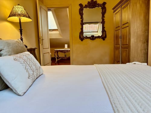 Elegante dormitorio en apartamento Lembrare de Baiona con paredes doradas, espejo ornamental y acceso a terraza con vistas al mar