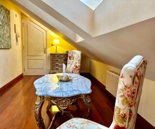 Elegante zona de estar en ático con mesa de mármol, muebles florales y claraboya en apartamento de Baiona