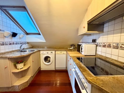 Moderna cocina de ático con lavadora, lavavajillas y encimeras de granito en apartamento frente al mar en Baiona