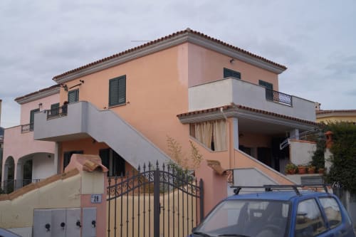 Sa Domo Mannoi Apartment in Orosei mit Terrakottamauern, weißen Balkonen und blauem Auto vor der Tür