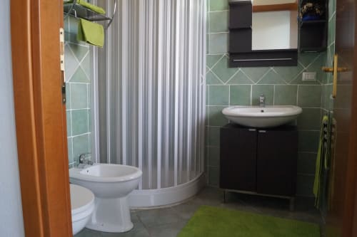 Modernes Badezimmer in der Wohnung in Orosei mit grünen Fliesenwänden, Dusche, Toilette und Waschbecken auf Säule