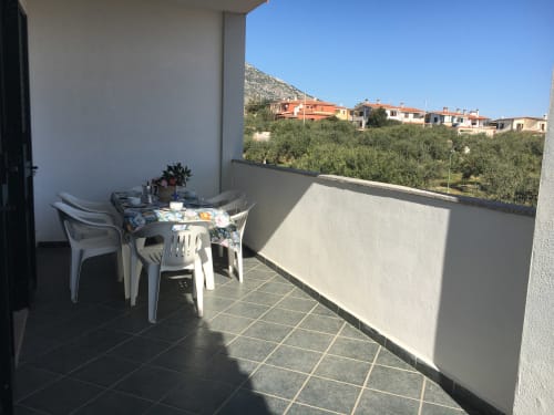 Sonnige Veranda mit weißen Möbeln mit Blick auf Olivenhaine und farbenfrohe Häuser in Orosei, Sardinien