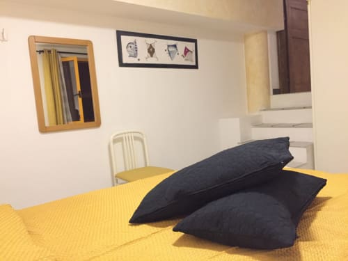 Bright bedroom in Casa Arborea apartment, Orosei, with yellow bed, black pillows, and neutral décor