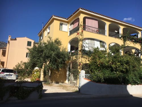 Yellow Mediterranean villa in Orosei with arched terraces, stone facade, and lush garden greenery