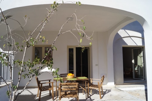 Outdoor veranda at Sa Domo De Mannoi in Orosei with dining table, wooden chairs, and young tree under curved white