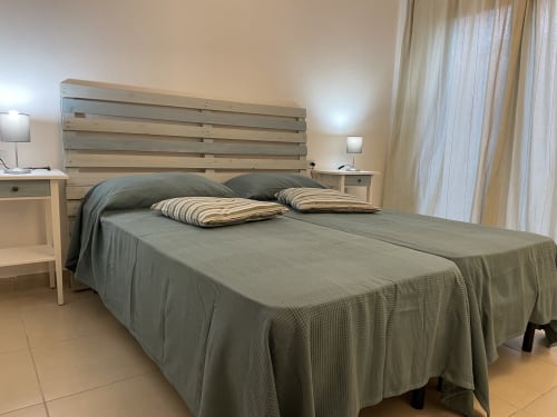 Modern bedroom in Orosei apartment with wooden slatted headboard, gray bedding, striped pillows, nightstands, and veranda