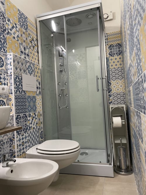 Modern bathroom with patterned blue and yellow tiles, walk-in shower, toilet, bidet, and sink in Orosei apartment