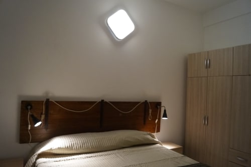 Modern bedroom at Sa Domo De Mannoi with wooden headboard, pillows, and ceiling light in Orosei apartment
