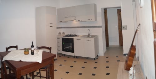 Modern kitchen-dining area in Orosei apartment with cream cabinets, gas cooktop, dining table, and decorative guitar