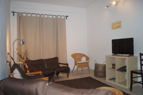 Modern apartment living room with sofa, armchair, TV, and beige curtains in Orosei, Italy