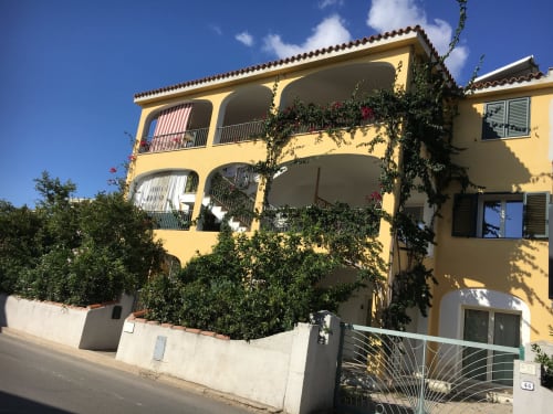 Bright yellow Mediterranean apartment building with curved balconies and ivy, Orosei Italy