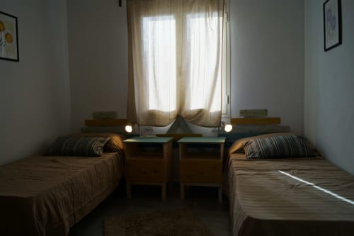 Twin bedroom in Orosei apartment with two single beds, bedside tables, lamps, and bright window with curtains