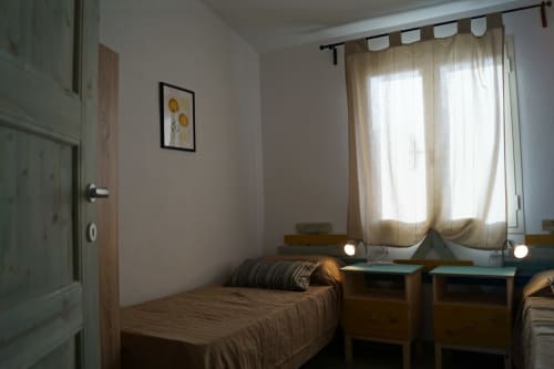 Bright bedroom at Domo De Mannoi in Orosei with single bed, wooden nightstands, large window with beige curtains