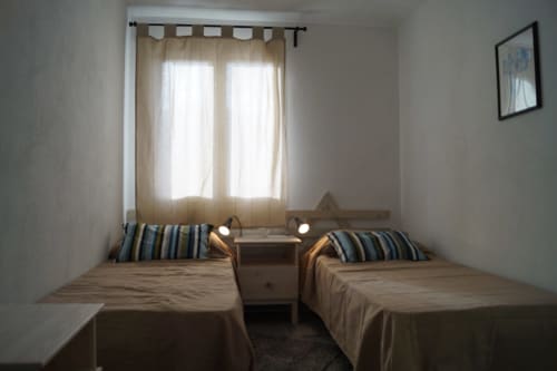Twin bedroom at Domo De Mannoi Alto in Orosei with striped pillows, wooden nightstand, and bright window with beige curtains