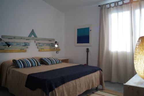 Cozy bedroom in Orosei apartment with striped pillows, coastal decor, and natural light from windows