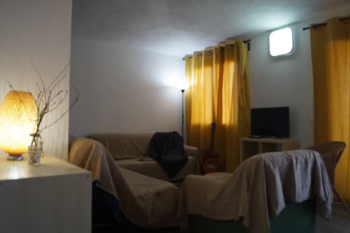 Cozy Orosei apartment living room with beige sofa, armchairs, yellow curtains, TV, and warm lamp lighting