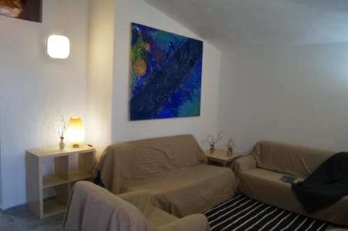 Cozy living room with beige armchairs, modern lighting, and abstract blue artwork in Orosei apartment