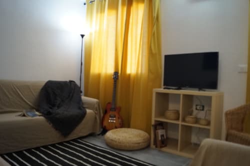 Cozy apartment living room in Orosei with sofa, red guitar, TV, yellow curtains, and striped rug
