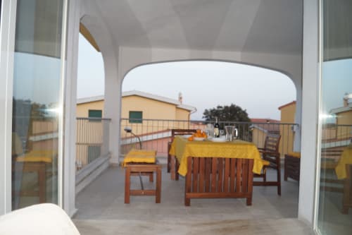 Spacious veranda at Domo De Mannoi in Orosei with wooden furniture, yellow tablecloth, and countryside views