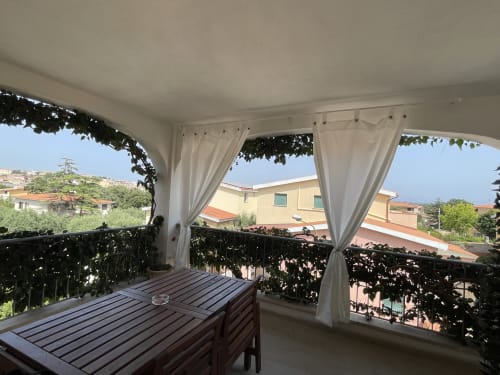 Covered veranda with white curtains, wooden dining table, city views in Orosei apartment