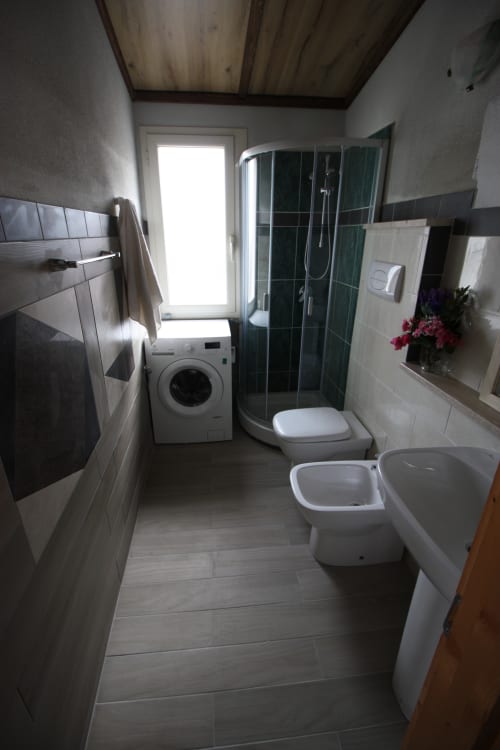 Modern bathroom in Sa Domo De Mannoi apartment, Orosei, featuring shower enclosure, toilet, bidet, washing machine, and tiled