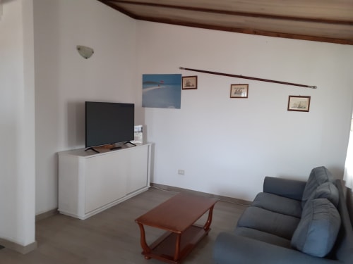 Living room with gray sofa, red table, TV on white cabinet, and framed artwork in Orosei apartment