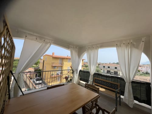 Covered veranda with white curtains, wooden dining furniture, and views of Orosei village and countryside