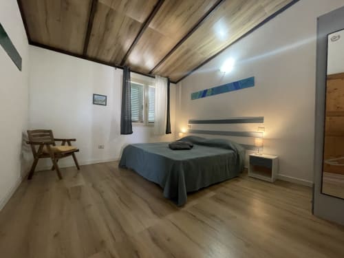 Modern bedroom in Sa Domo De Mannoi apartment, Orosei with queen bed, wooden ceiling, desk chair, and ambient lighting