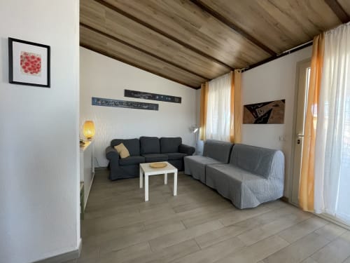 Modern living room with black sofa and gray seating, wooden beamed ceiling, white walls at Sa Domo De Mannoi apartment in