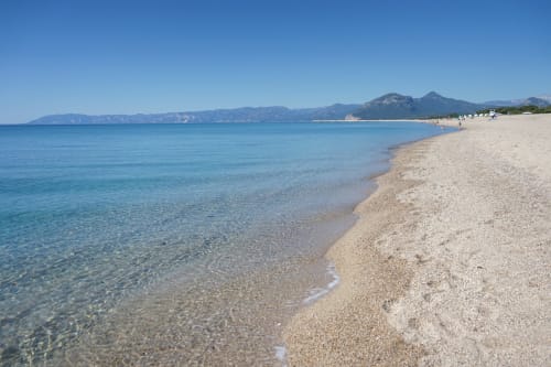 Pristine sandy beach with crystal-clear turquoise water and mountains in background, Orosei, Italy