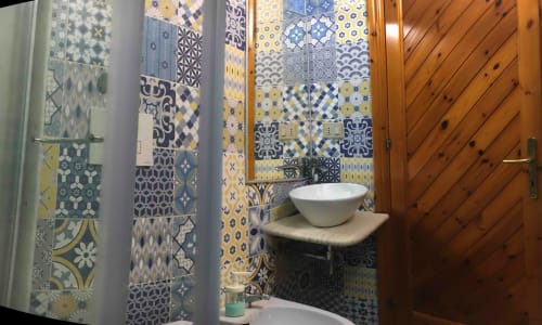Bagno moderno con piastrelle decorative a motivi geometrici blu, gialli e bianchi, lavabo a bacinella e porta in legno a Casa Arborea