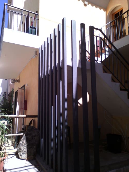 Cortile moderno con divisorio in stecche nere, muri in terracotta e ringhiere metalliche nella proprietà Loddo Paola a Orosei
